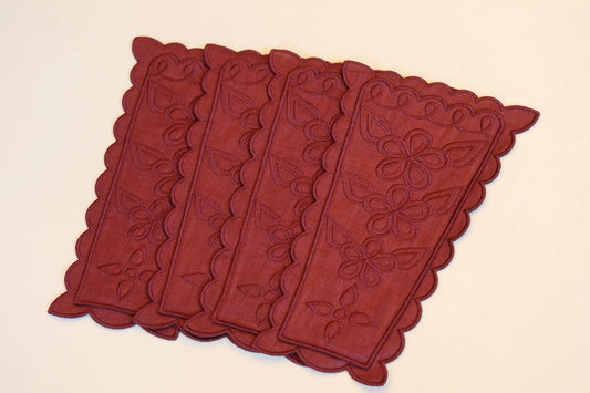 Range-couverts en lin couleur prune, décorés de broderies florales et de bords festonnés, disposés en éventail sur fond clair.